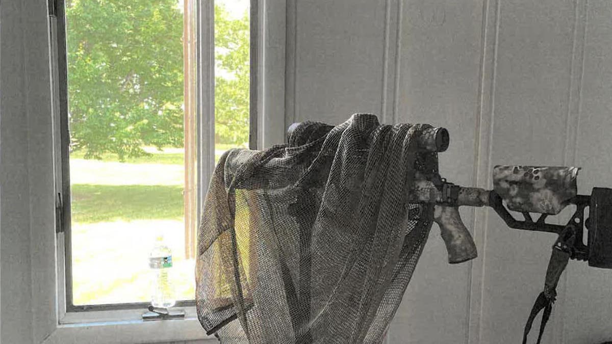 A sniper's rifle camouflaged as it angles out a window