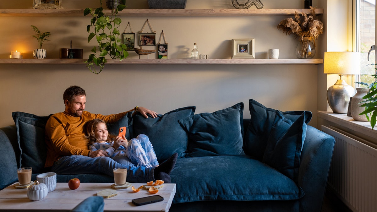 Father lying down on the sofa with his daughter on her phone