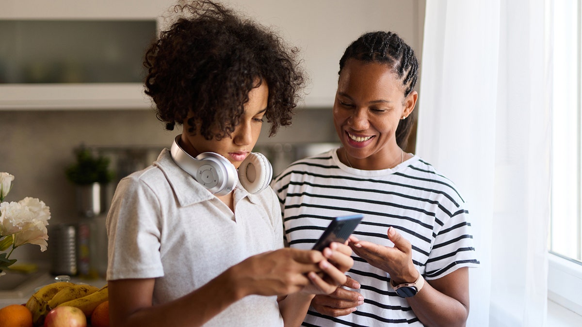 Teenage boy and his mother using smart phone at home