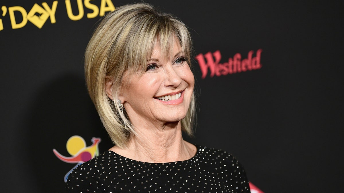 Olivia Newton John smiles and looks up on the carpet