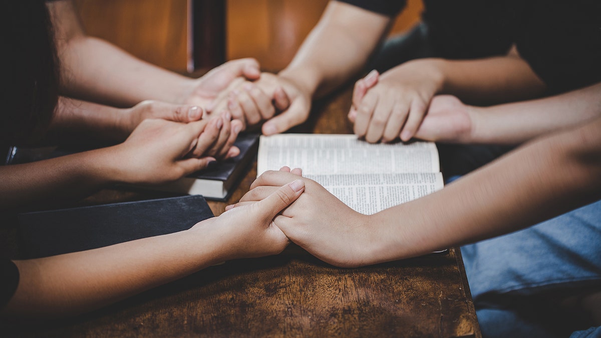 Group praying around a table with a Bible