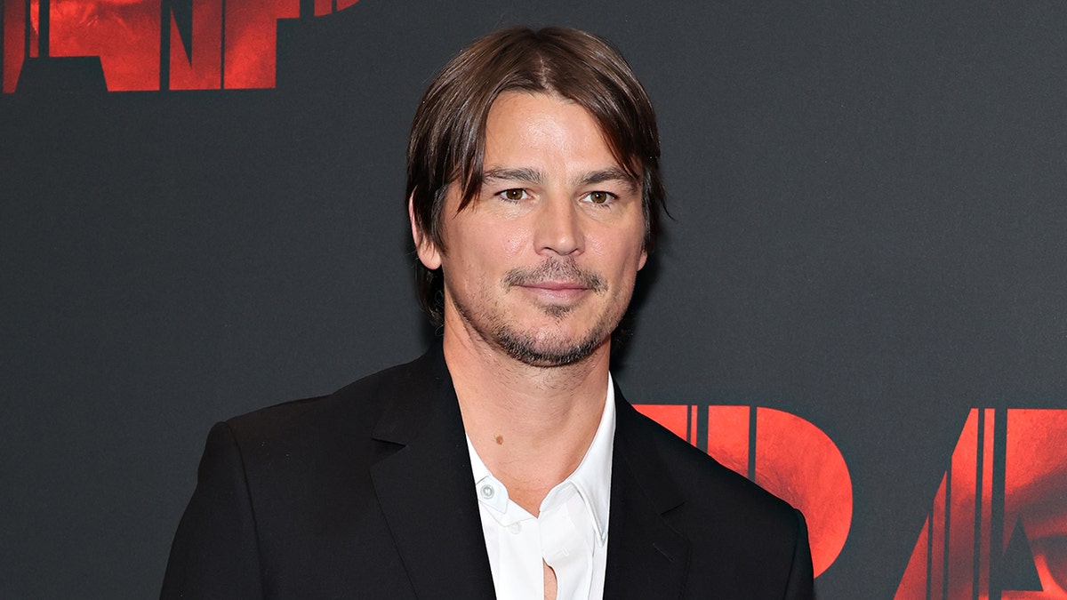 Actor Josh Hartnett smiles wearing a black suit and white shirt.