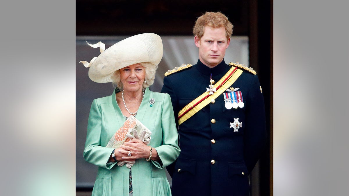 Queen Camilla in a green dress and beige hat next to Prince Harry in military attire, appearing displeased.