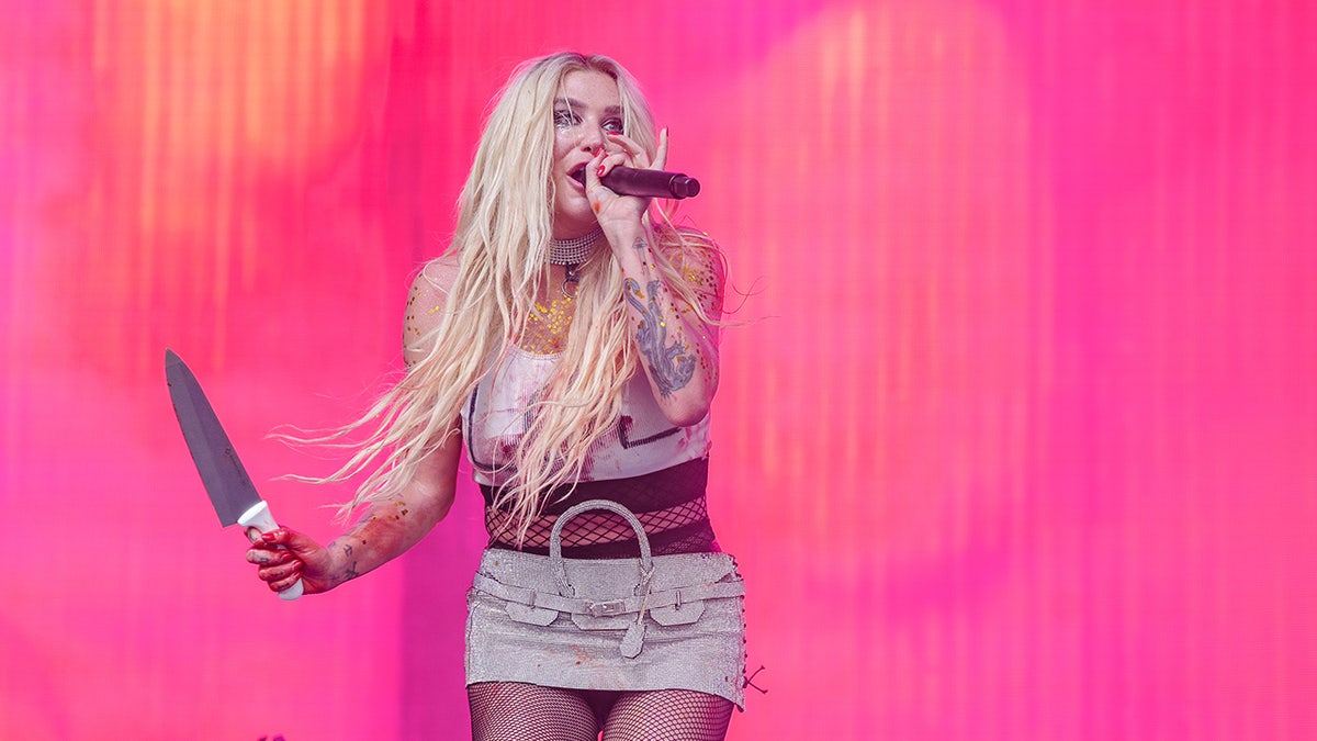 Kesha performs at Lollapalooza, holding a knife in one hand while singing into a microphone with the other.