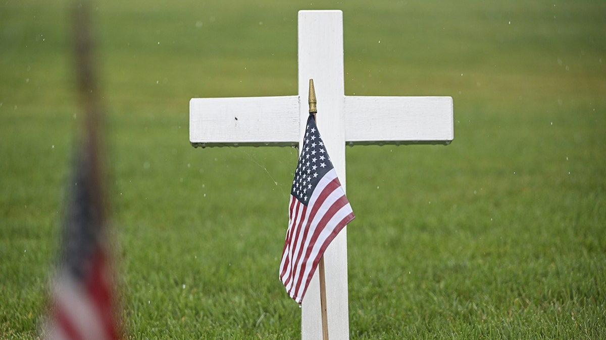 An American flag at a veteran's grave, marked by a cross