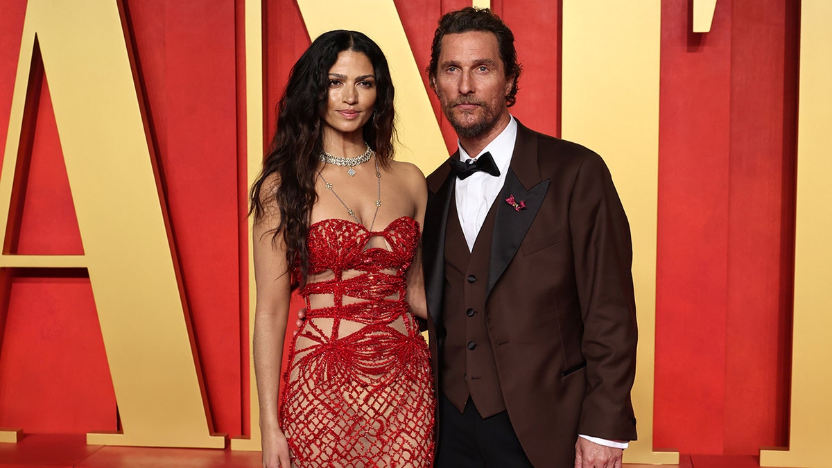 Camila McConaughey in a red beaded strapless dress poses with her husband Matthew McConaughey in a dark suit at the Vanity Fair after party