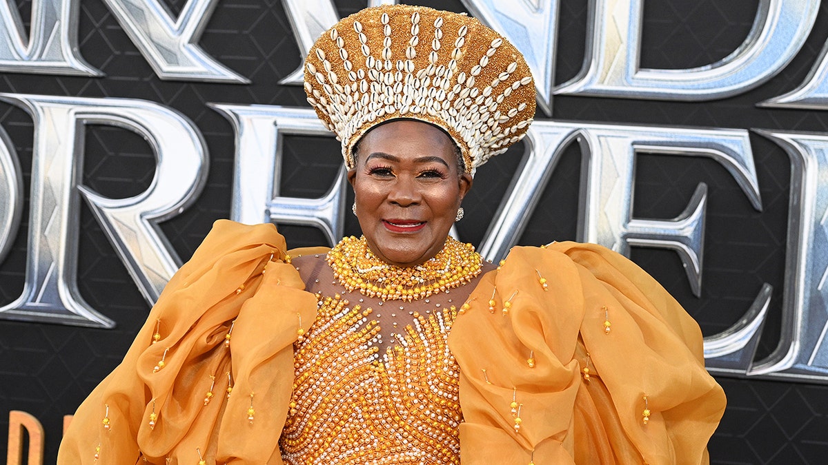 Connie Chiume in a golden yellow dress with puffy sleeves and a matching headpiece at the "Wakanda Forever" premiere