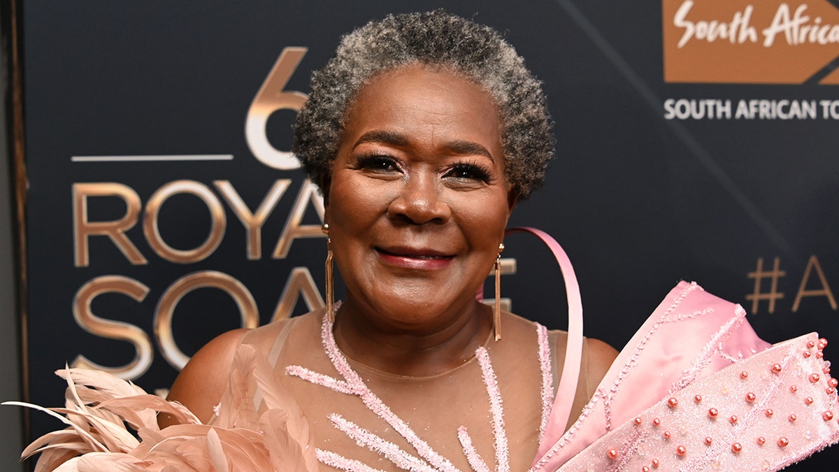 Connie Chiume in an ornate pink dress smiles on the carpet in South Africa