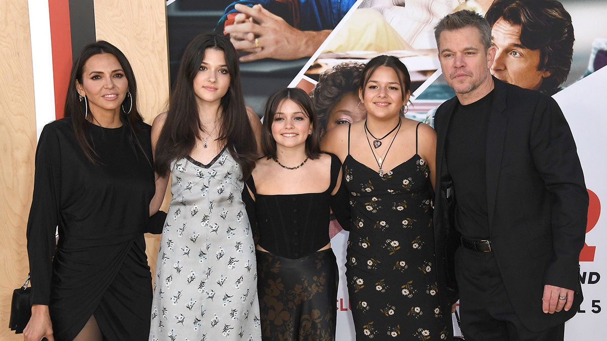 Luciana Damon in black poses for a photo at the premiere with daughters Isabella, Stella, Gia, and husband Matt Damon in a black suit