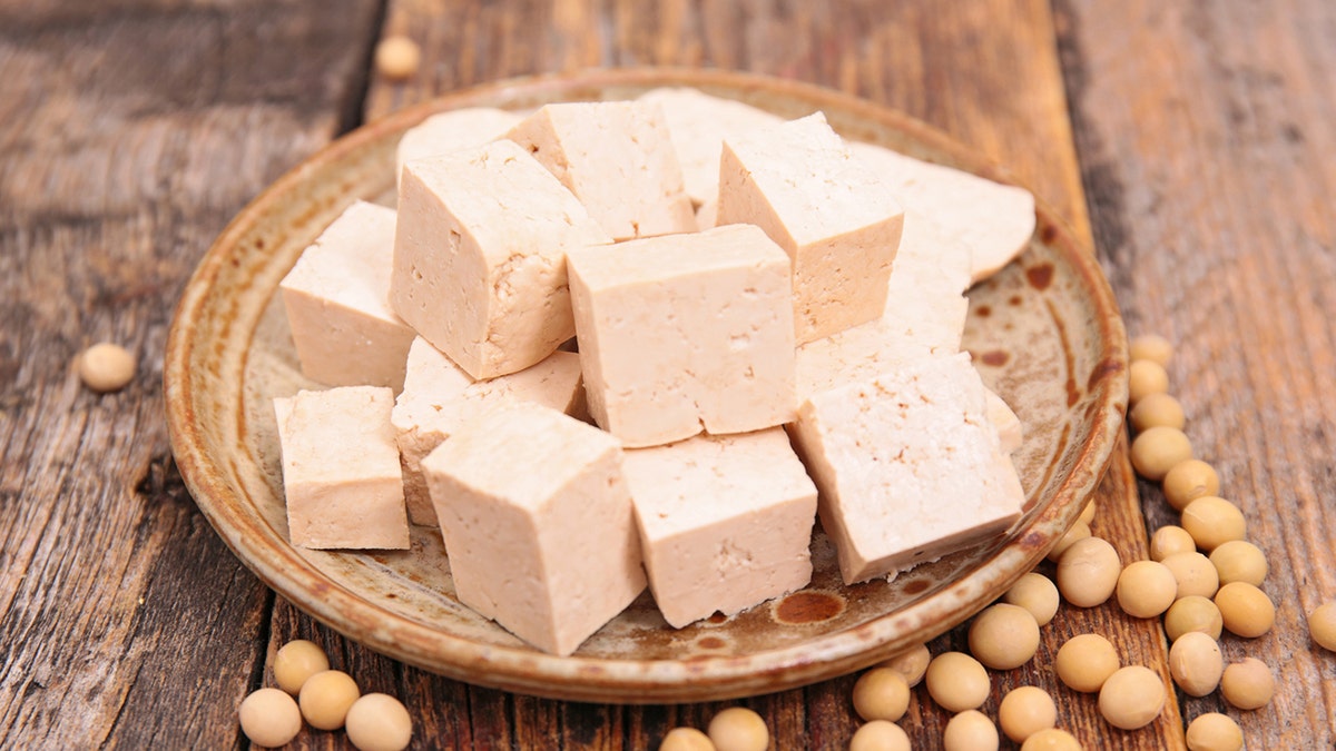 Squares of tofu on a plate alongside soybeans.