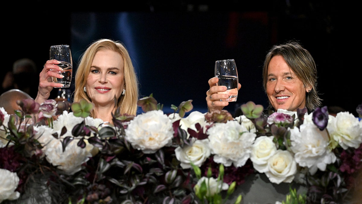 Nicole Kidman and Keith Urban clink glasses behind a floral arrangement