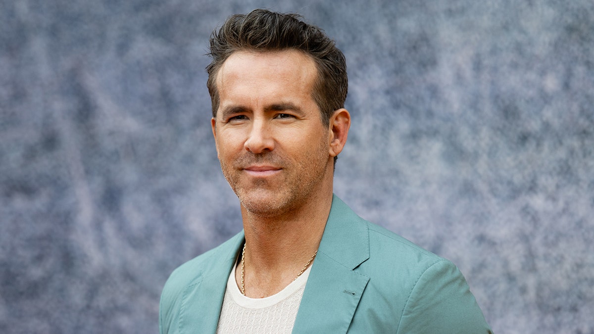 Ryan Reynolds in a turquoise blazer with a soft smile on the carpet